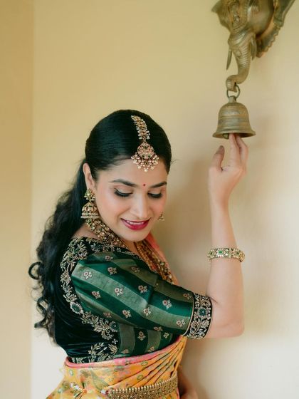 The traditional bell and the bride's elegant pose evoke a sense of timeless heritage. Her saree is a perfect match for the classic ambiance.