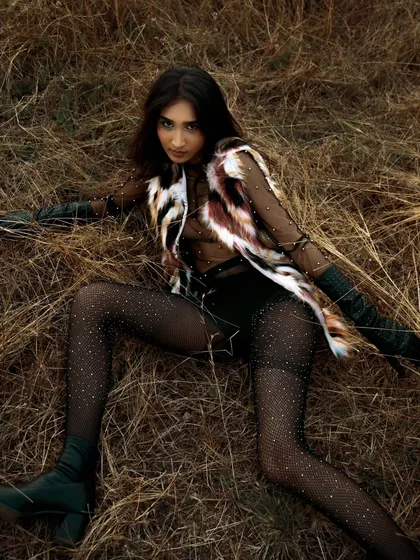 A dynamic, reclining pose from the same outdoor editorial. The textures of the clothing and the dry grass create a rich, tactile image.
