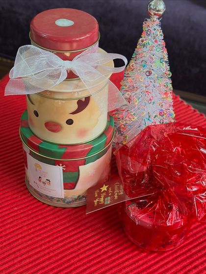 Our Christmas tins stacked and ready for gifting. The snowman and Santa-themed tins are tied with a bow, making them a delightful present for friends and family during the holidays.