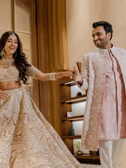 A joyful, candid moment of the couple twirling. Her intricately embroidered lehenga and his classic pink and white sherwani are a perfect match.