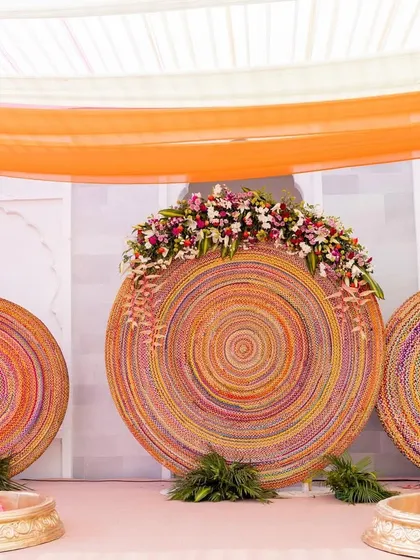 The main stage for the Haldi ceremony, featuring large, colorful circular backdrops made of woven materials and adorned with flowers.