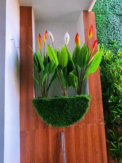 This wall-mounted planter is a piece of art. It features a base of artificial grass with vibrant, realistic-looking peace lilies, adding a pop of color to a wood-paneled wall.