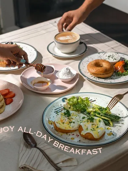 My all-day breakfast menu allows you to enjoy your favorites anytime. This spread shows eggs benedict, pancakes, and a bagel with salmon, shared among friends.