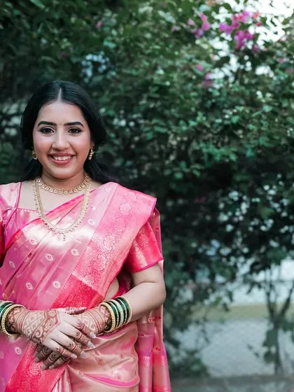 A beautiful portrait of a bride in a pink saree against a natural green background.