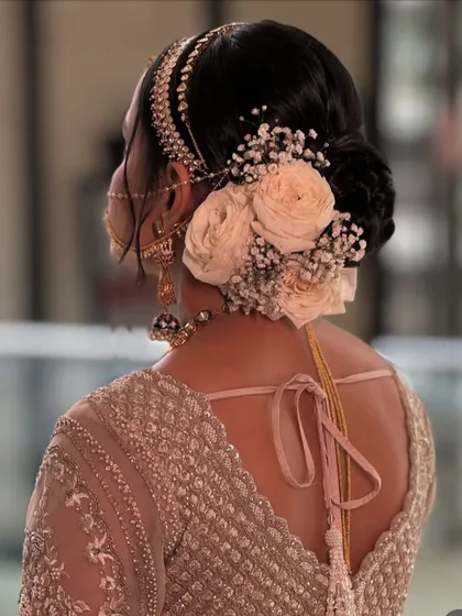 A beautiful bridal bun featuring a combination of fresh baby's breath and soft peach roses. This style is perfect for brides who want a romantic and elegant updo that complements a pastel or neutral-toned lehenga.