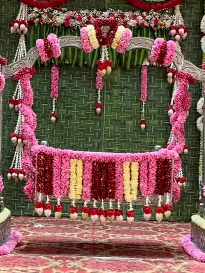A detailed view of one of my silver cradles (thottilu) available for rent, decorated for a naming ceremony. I've adorned it with dense garlands of pink and red roses against a backdrop of woven banana leaves, perfect for a traditional event.