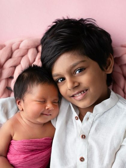 The sweet smile on a newborn's face as her big brother holds her close. A perfect capture of sibling love from the very beginning.
