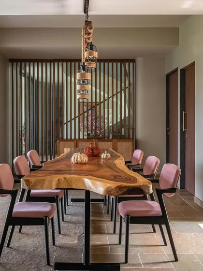 The dining area at Grove House features a stunning live-edge wooden table paired with modern pink velvet chairs. This mix of rustic and contemporary elements creates a vibrant and welcoming space for family meals at this Alibaug retreat.