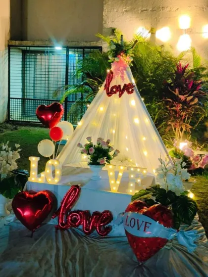 An outdoor cabana tent setup for a romantic occasion. Decorated with "LOVE" marquee letters and red heart balloons, it's perfect for an anniversary or Valentine's surprise.
