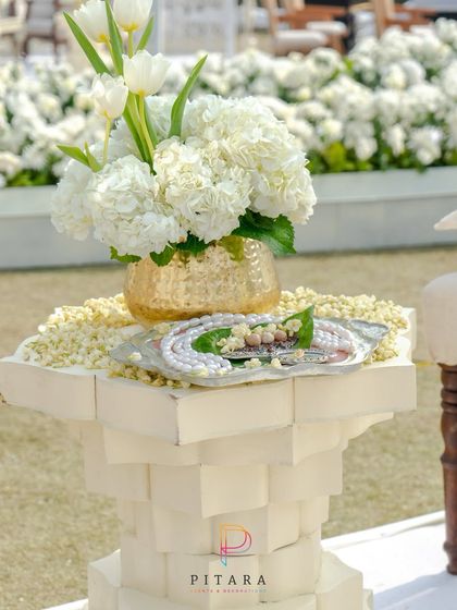 A simple yet elegant detail: a modern white pedestal holding a traditional welcome tray and a golden vase of white hydrangeas.