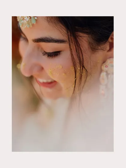 A soft, beautiful close-up of the bride with a touch of Haldi on her cheek, smiling gently.