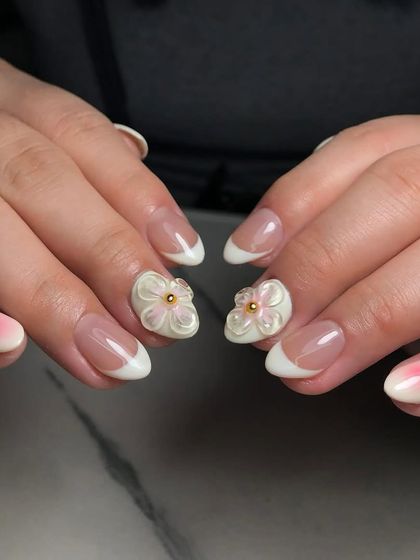 A delicate French manicure base elevated with 3D sculpted flowers and a touch of blush. This is a perfect example of modern bridal or special occasion nail art.