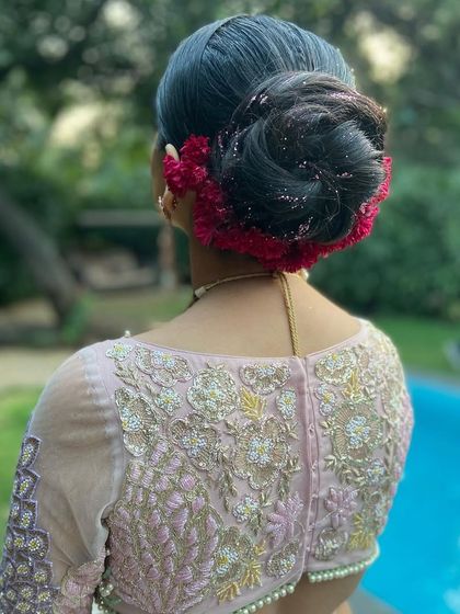 A high bridal bun wrapped in vibrant red coxcomb flowers. The unique texture of these flowers adds a rich, velvety look to the hairstyle.