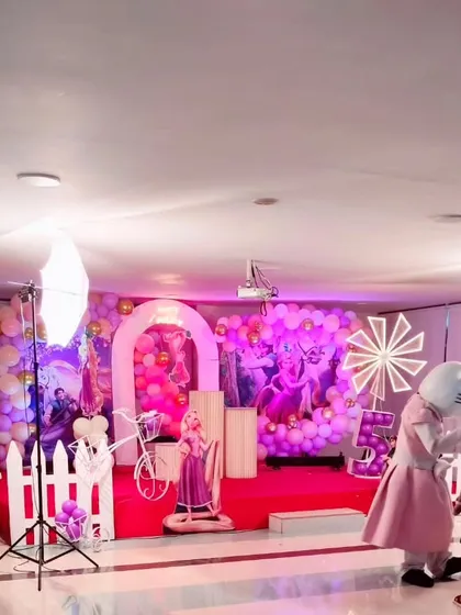A wide shot of a princess themed party in progress, showing the decorated stage and a mascot character entertaining the children.