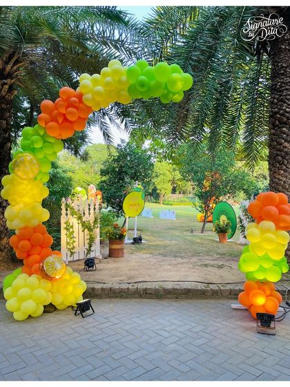 A citrus-coloured balloon archway welcomes guests to the 'Two-tti Fruity' party. The arch frames the beautiful outdoor lawn setting, hinting at the fun and games waiting inside.