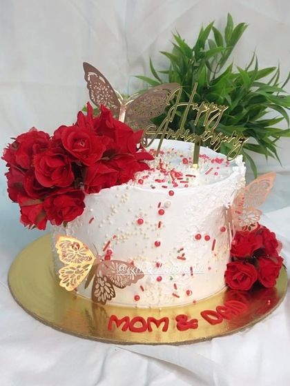 A timeless combination of red and white for a pretty floral anniversary cake. This design uses whipped cream frosting, red roses, and delicate gold butterflies for a classic and romantic feel.