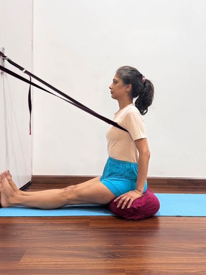 Using a belt from a wall hook to assist in Dandasana. This provides traction and helps to lift the spine, making the subsequent forward bend more effective and safe.