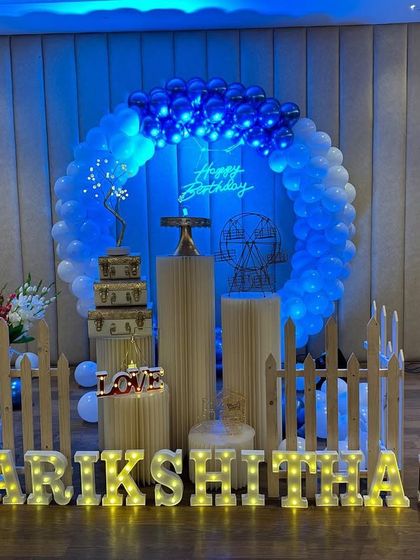 A beautiful blue-themed setup with a circular balloon arch and a neon sign. The decor includes elegant plinths and a picket fence for a charming touch.