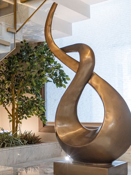 A tall, slender faux tree is paired with a modern bronze sculpture, creating a sophisticated art and nature installation. This design demonstrates how we blend greenery with other decor elements.