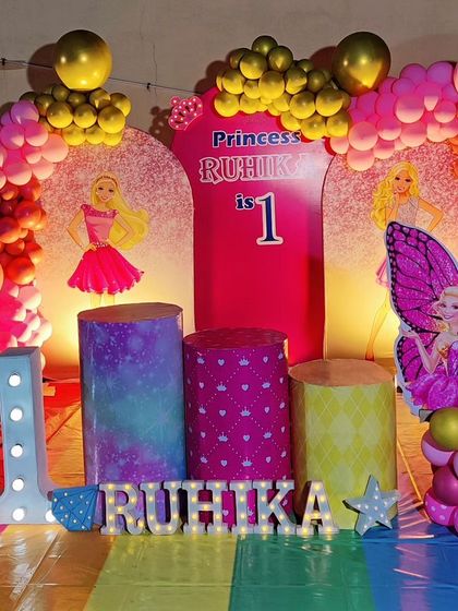 A full-stage princess-themed first birthday. The decor includes a rainbow-colored floor, princess cutouts, and a large light-up number '1'.