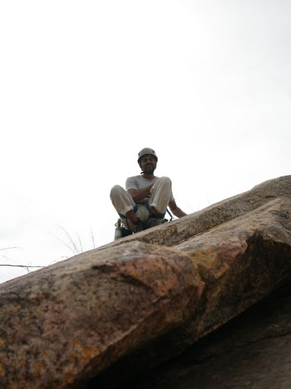 A climber smiles from the top of a rock, enjoying the feeling of accomplishment and the view. This is what it's all about.