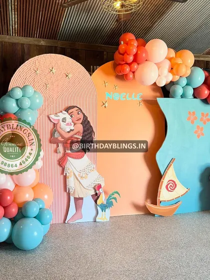 A warm and inviting Moana theme with orange, pink, and teal balloons. The setup includes cutouts of Moana, Pua, and Heihei, along with a sailboat prop.