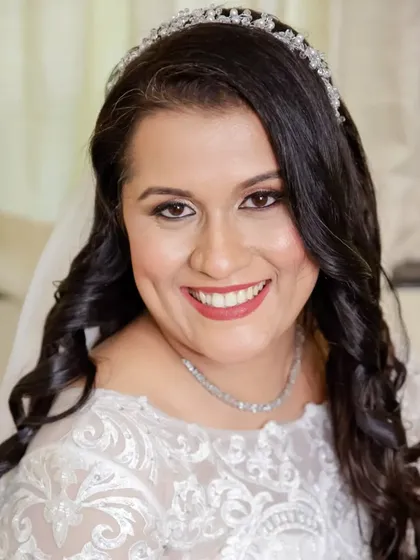A happy and confident bride, ready for her ceremony. The makeup is classic and clean, with defined eyes and a warm red lip, paired with soft curls and a delicate tiara.