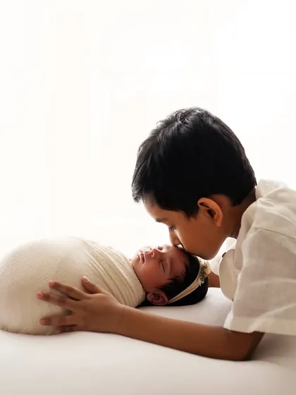 A tender moment as a big brother leans in to give his new baby sister a kiss on the forehead. My heart melts every time.