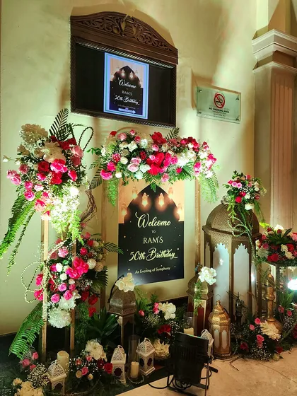 A personalized welcome for a 50th birthday celebration with a Sufi Night theme. The entrance features a custom sign, ornate Moroccan-style lanterns, and beautiful arrangements of red and pink roses.
