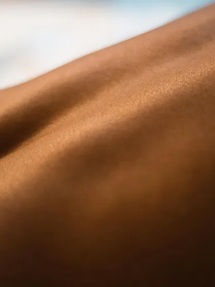 A macro-style fine art photograph capturing the texture and landscape of skin. The warm light highlights the subtle contours of the human form.