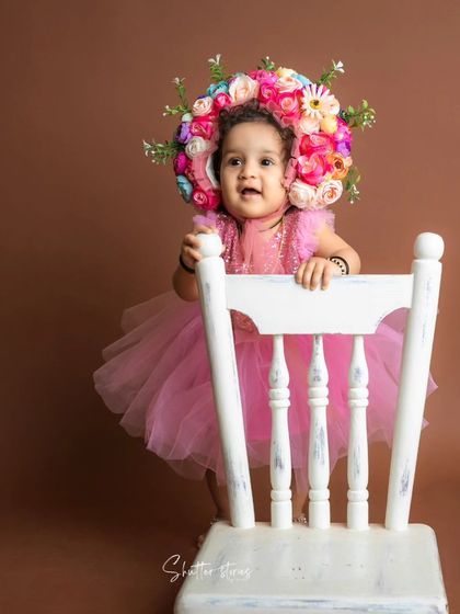 Standing tall! This one-year-old proudly holds onto a white chair, showing off her new skills.