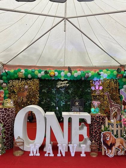 A large-scale jungle theme set up inside a tent for an outdoor party. This decoration includes a full balloon arch, a shimmer wall, large 'ONE' letters, and plenty of safari animal cutouts.