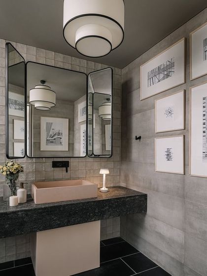 A detail from the powder room, featuring a pink concrete sink against a backdrop of grey tiles and framed art, showcasing a unique color and material combination.