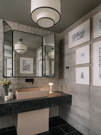 This bathroom features a unique combination of materials, with a pink concrete sink set against a dark stone countertop and grey tiles. The framed art adds a personal, gallery-like feel.
