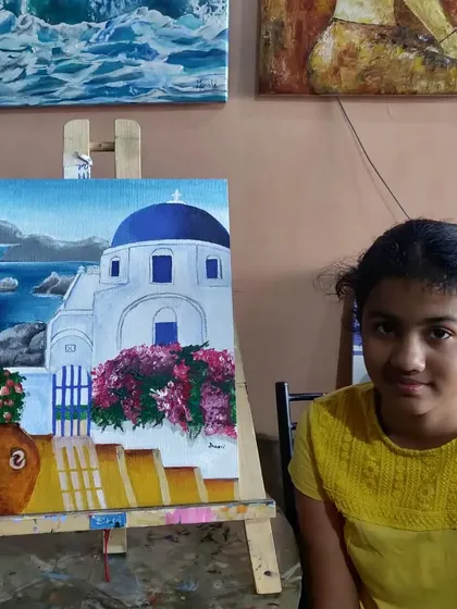 A teen student with her completed painting of Santorini. This popular subject is a great way to practice painting architecture, vibrant colors, and the contrast between the white buildings and the blue sea.