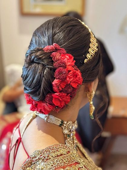 A side profile of the intricate red floral bun. You can see the texture of the bun and how the flowers are layered to create depth, perfectly complementing the bride's traditional jewellery.