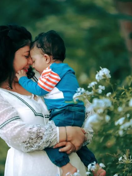 A tender moment between mother and child, captured against a backdrop of soft white flowers. The natural lighting enhances the warmth of the scene.