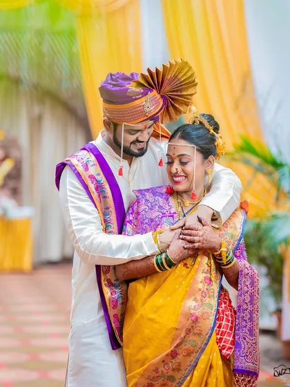 A joyful embrace between the bride and groom, showcasing the vibrant yellow and purple of their traditional Maharashtrian wedding outfits.