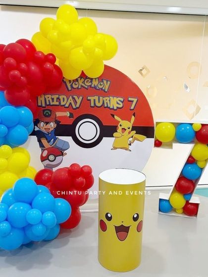 A Pokemon-themed 7th birthday party featuring a Pokeball backdrop with Ash and Pikachu. The decor includes a balloon-filled marquee number '7' and a Pikachu-themed pedestal.
