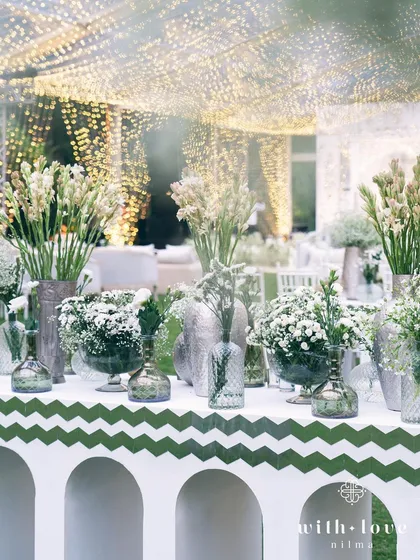 A bar setup with an assortment of white flowers under the fairy-lit tent. The design ensures that every corner of the event is visually stunning.