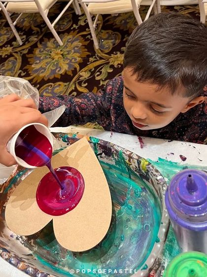 Even our littlest artists can join in. A young boy gets hands-on with pouring vibrant purple and pink paint onto a heart canvas at a birthday party.