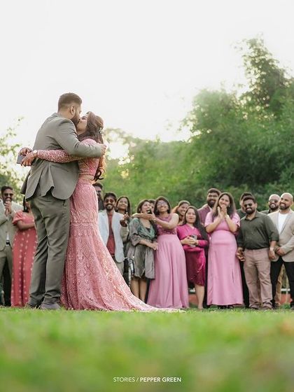 The first kiss as husband and wife, with friends and family cheering in the background. This wide shot captures the collective joy of the moment.