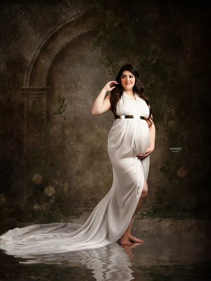 A classic fine art portrait against a dark, textured backdrop. The simple white gown and the water reflection effect create a moody, elegant, and timeless image.