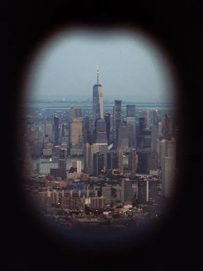 A voyeuristic view of the downtown Manhattan skyline, seen through a binocular viewer. This framing adds a sense of distance and observation.