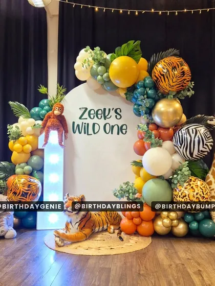 A "Wild One" jungle theme with a variety of plush animal props like a tiger, elephant, and giraffe. The setup includes a light-up number '1' and a balloon garland with tiger and zebra-print accent balloons.