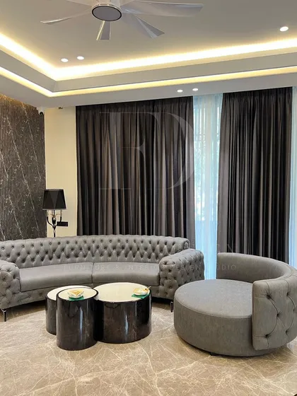 Timeless elegance meets modern comfort. This living space features a classic tufted Chesterfield sofa and a curved accent chair, set against a backdrop of dramatic marble walls and sophisticated cove lighting, creating a warm and inviting atmosphere.