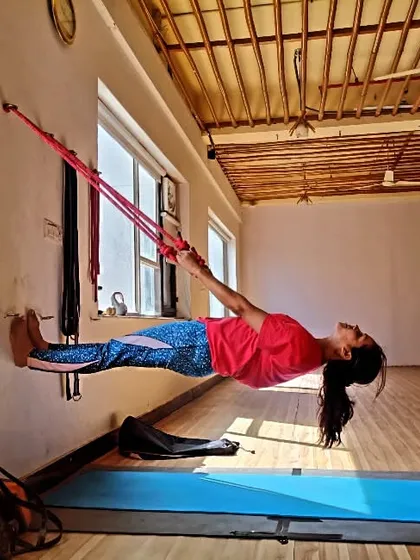 A student demonstrates incredible core strength by holding a horizontal plank supported only by her feet on the wall and hands in yoga ropes. This is an advanced wall rope yoga technique.