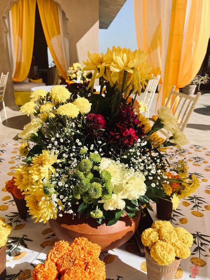 A Haldi centerpiece combining marigolds, chrysanthemums, and baby's breath in a terracotta pot, set on a block-printed table linen.