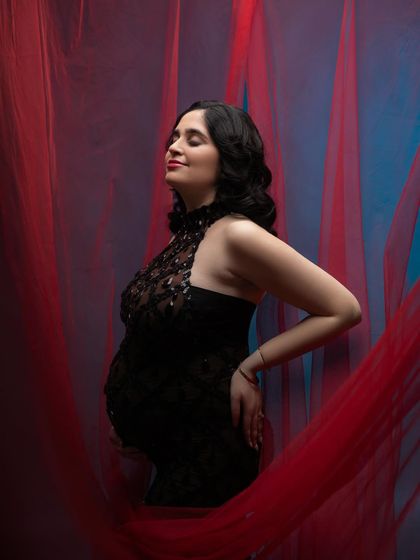 The sheer red fabric adds a layer of softness and movement to this glamorous portrait, contrasting beautifully with the sparkling black gown.