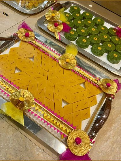 A close-up of our decorative wedding sweet trays, featuring mango barfi and pista rolls. The presentation is enhanced with festive gota patti work, perfect for traditional ceremonies.